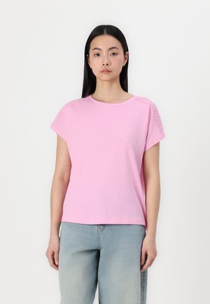 Rosa kortärmad t-shirt i mjukt material med ögla detaljer på axlarna. Avslappnad passform och rund halsringning. Kombinerad med ljusa jeans.
