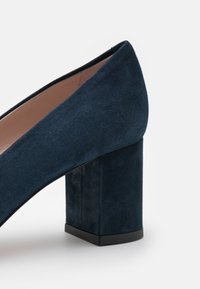 Chaussure à talon haut en daim bleu marine avec un talon bloc carré, présentant une texture lisse et une silhouette élégante.