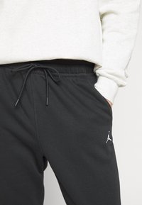Svarta joggerbyxor i mjukt tyg, med elastisk midja och dragsko, samt en vit logotypaccent på vänster lår.