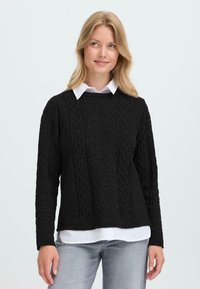 Maglione nero a maglia cable con scollatura rotonda e maniche lunghe, indossato sopra una camicia bianca con colletto. Tessuto morbido e vestibilità rilassata.