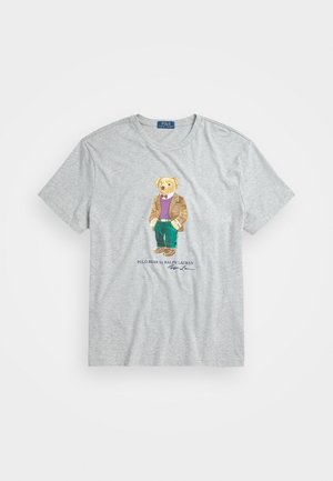 Hellgraues T-Shirt mit einer Grafik eines Bären, der eine braune Jacke, einen violetten Pullover, grüne Hosen und braune Schuhe trägt, beschriftet Polo Bear von Ralph Lauren.