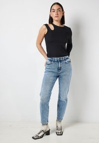 Zwarte geribde langemouwen top met een uitsnijding op de schouder, gecombineerd met lichtblauwe high-waisted jeans en kniehoge slangenprint haklaarzen.