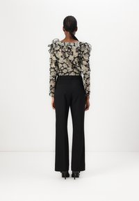 Zwarte bloemenblouse van doorschijnende stof met ruches aan de mouwen, gecombineerd met hooggepaste zwarte broeken en hakken. Op maat gemaakte pasvorm.