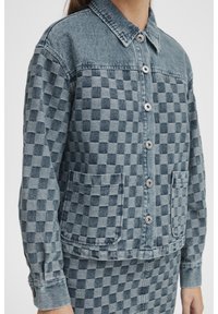 Kraciasta kurtka dżinsowa w odcieniach niebieskiego, z kołnierzem, guzikami z przodu i dwoma naszywanymi kieszeniami. Casualowy krój z długimi rękawami.