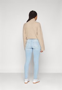 Suéter de punto beige con cuello alto, jeans ajustados azul claro y zapatillas blancas. Textura suave, corte relajado y diseño simple.