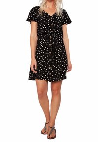 Robe noire à manches courtes, motif floral blanc, boutons sur le devant et détail de taille nouée, associée à des sandales plates noires.