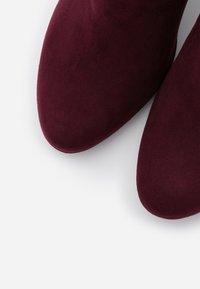 Burgundské kotníkové boty vyrobené z jemné semišové kůže s kulatou špičkou, s hladkým povrchem a bezproblémovým designem.