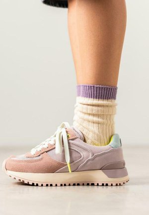 Baskets de course en suède violet clair et rose, avec des lacets blancs, une semelle empilée et une touche de jaune. Portées avec des chaussettes rayées crème et lavande.