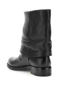 Bota de cuero negra hasta la mitad de la pantorrilla con un eje ligeramente caído y un tacón bajo apilado, mostrada desde un ángulo trasero de tres cuartos.