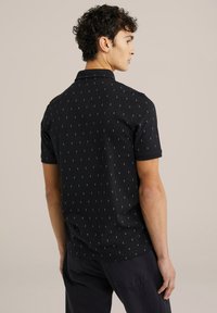 Cămașă polo neagră cu un model texturat format din forme albe mici, cu mâneci scurte și guler clasic. Materialul pare moale și ușor.