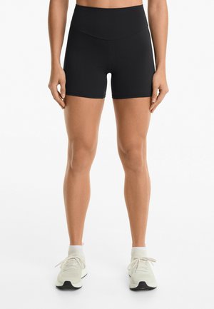 Pantaloni sportivi neri a vita alta in un tessuto texturizzato, design aderente, che arrivano a metà coscia, abbinati a scarpe da corsa grigio chiaro.
