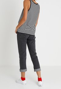 Randig svart och vit ärmlös topp, mörkgrå jeans med uppvickade ärmar, och vita sneakers med röda ankelsockor, sedd bakifrån.