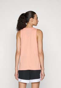 Sleeveless peach tank top with a slight V-cut at the back, featuring a soft texture. Paired with black shorts and a white hem.