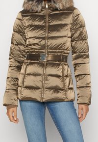Chaqueta acolchada bronce con cremallera frontal, patrón acolchado, capucha forrada de pelo y cinturón de tela. Material texturizado y brillante con bolsillos laterales.