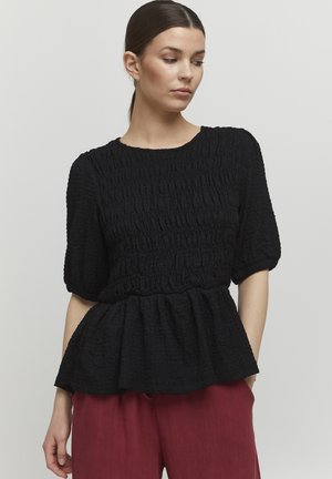Schwarze strukturierte Bluse mit kurzen Puffärmeln und einem Peplum-Saum. Verfügt über einen runden Ausschnitt und geraffte Stoffdetails. Getragen mit roten Hosen.
