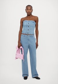 Lyseblå denim strapless topp med frontknapper, kombinert med vide jeans. Holder en rosa teksturert håndveske med bueaksent.