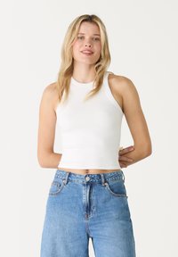 Hvid, ribbet cropped tanktop med rund halsudskæring og ærmeløs design, parret med højtaljede lyseblå denimjeans.