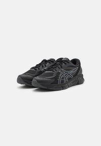 Chaussures de sport noires avec une tige en mesh, surface texturée et accents argentés réfléchissants. Bout arrondi et conception de semelle rembourrée et moulée.