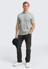 T-shirt à manches courtes rayé en gris clair avec des rayures sombres et pastel, associé à un jean foncé et des baskets blanches, tenant une casquette marine.