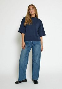 Un haut oversize navy à manches courtes, associé à un jean large bleu clair. Le jean présente une texture denim classique et des poches avant.