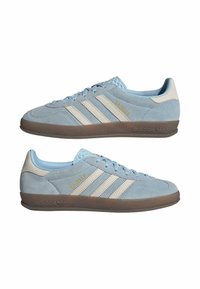 Gaiši zili zamšādas kedas ar baltām ādas detaļām, kurās ir trīs baltas svītras un zeltīšana "Gazelle" emblēma sānos. Gumijas zole.