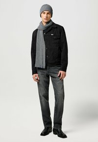 Giubbotto di jeans neri sopra una camicia nera, sciarpa a coste grigia, berretto grigio, jeans grigio scuro e stivaletti neri alla caviglia. Design semplice e urbano.