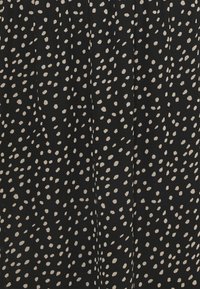 Svart tyg med en texturerad yta, med ett genomgående mönster av vita prickar. Prickarna varierar i storlek och är oregelbundet placerade.