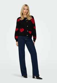 Svart kavaj med röda hjärt-mönster, långa ärmar och knäppning. Bärs över mörkblå vida jeans och svarta klackstövlar.