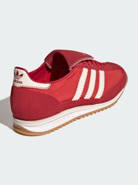 Červená športová obuv s vrchnou časťou zo zamatovej a textilnej látky, tromi bielymi pruhmi a podrážkou z gumy vo farbe prírodného kaučuku s vystlaným golierom pre pohodlie.