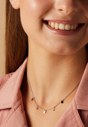Silver chain necklace with small rectangular pendants and round accents, worn on a tanned neck, with a pink collared shirt in the background.