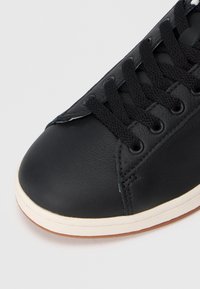 Μαύρο δερμάτινο αθλητικό παπούτσι με στρογγυλή μύτη, επίπεδες μαύρες κορδόνες και λευκή σόλα. Υφασμάτινος δερμάτινος επάνω μέρος με λεπτομέρειες ραφής.