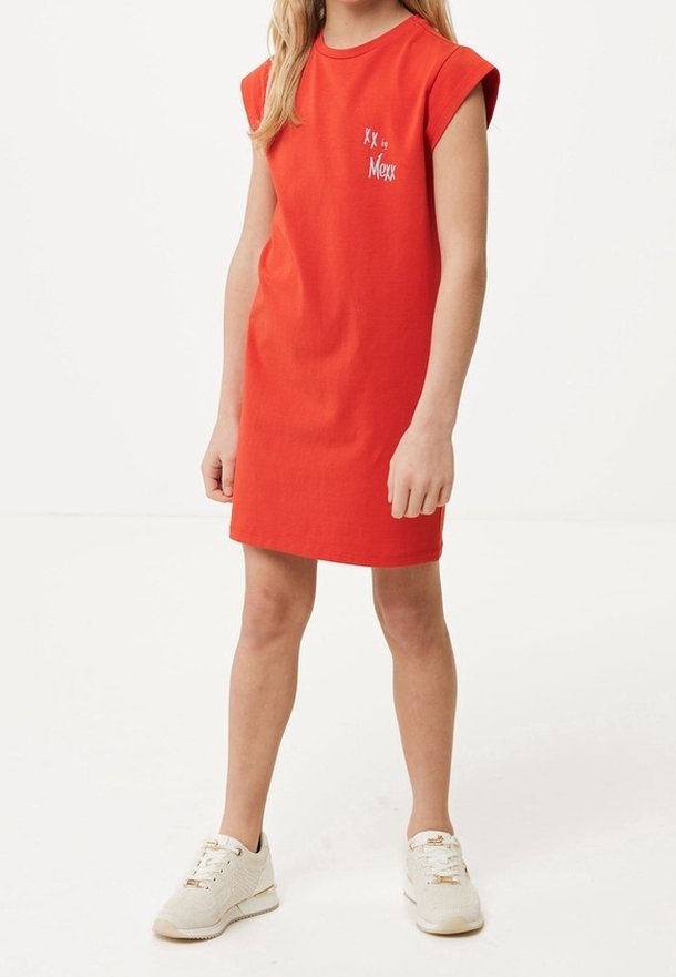 Enfant portant une robe rouge à manches courtes et des baskets blanches, debout devant un fond blanc uni.