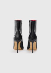 Sorte læder ankelstøvler med lynlås, høje stilettohæle og rød indvendig foring. Elegant design med glat tekstur.