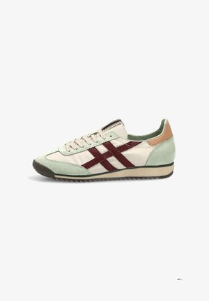 Zapatilla de perfil bajo con tela beige, detalles en ante verde menta, rayas de cuero granate, parche en el talón color canela y cordones beige sobre fondo blanco.