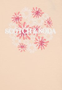 Persiku krāsas T-krekls ar ziedu grafiku rozā un baltā krāsā, ar zīmola nosaukumu "SCOTCH & SODA" drukātu treknā baltā tekstā.
