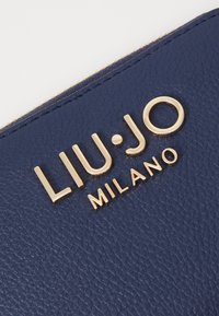 Portafoglio in pelle blu navy con logo in oro embossato "LIU·JO MILANO", dotato di superficie testurizzata e dettagli in oro sulla zip.