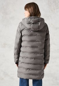 Abrigo acolchado gris ligero con capucha, que presenta patrones de acolchado horizontales y puños elásticos, terminado por debajo de las caderas.