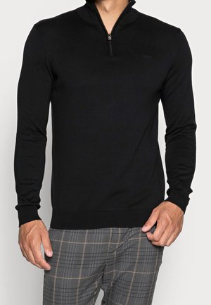 Schwarzer Pullover mit einem Viertelreißverschluss-Kragen, gerippten Bündchen und Saum. Weicher Stoff und taillierte Passform, kombiniert mit karierten Hosen.