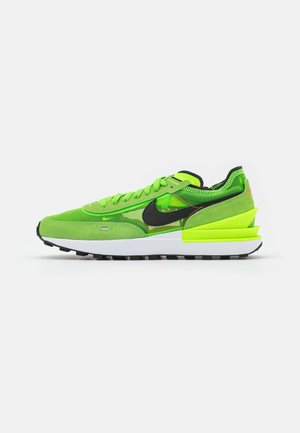 Felgroene Nike sneaker met zwarte swoosh, gelaagde zool, bovenwerk van mesh en suède en neongele accenten, zijaanzicht op een witte achtergrond.