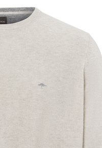 Helle beigefarbene Rundhals-Strickjacke aus weichem Material. Verfügt über ein dezent blaues Logo-Detail auf der Brust und einen gerippten Halsausschnitt.