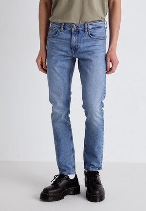 Light blue denim jeans with a straight fit and five-pocket design. Worn with black platform shoes, set against a plain background.
