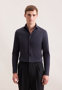 Blusa blu navy con maniche lunghe e chiusura a bottoni, realizzata in un tessuto liscio. Presenta un colletto classico e una leggera lucentezza.