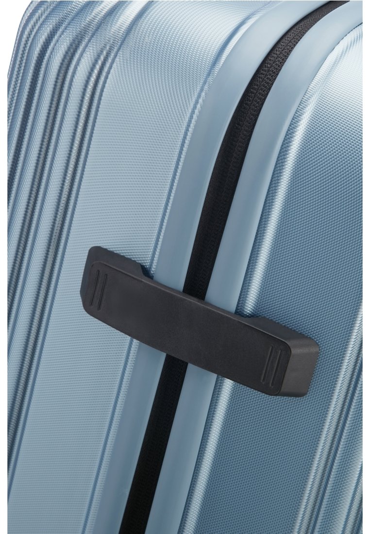 Valise rigide texturée bleu clair avec une poignée latérale noire et une fermeture éclair noire visible courant le long du bord.