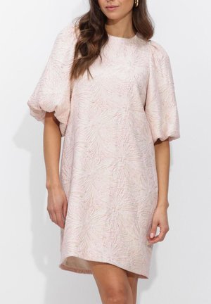 Vrouw draagt een knielange, lichtroze textuurrijke jurk met opgeblazen korte mouwen en een ronde halslijn.