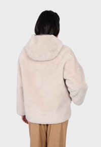 Beżowa kurtka z sztucznego futra z dużym kapturem, oversize'owy krój, długie rękawy i miękka tekstura, widok z tyłu.