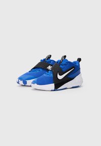 Zapatos deportivos azules con una correa negra, parte superior de malla texturizada, suela blanca y logo de Nike prominente en negro. Presentan puntera reforzada.