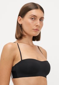 Black strapless bra with adjustable thin straps, smooth texture, and side mesh detail featuring white stripes for added design.