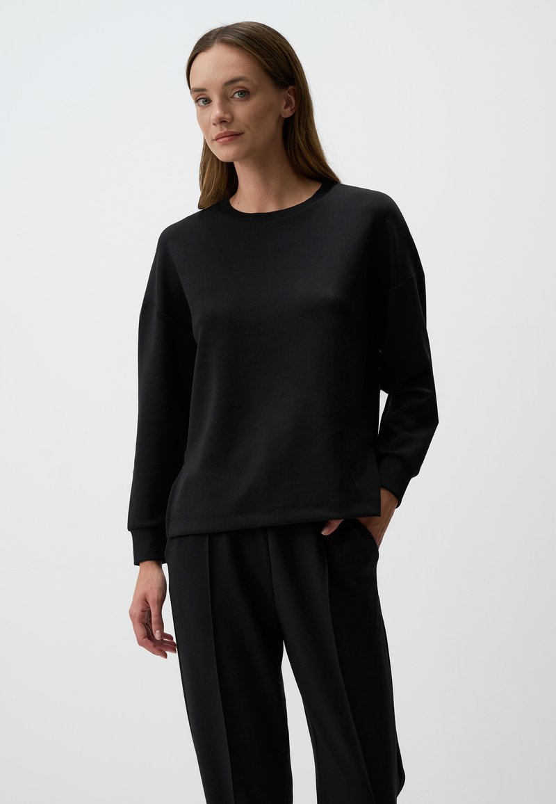 Felpa nera con colletto rotondo, maniche lunghe e vestibilità comoda. Realizzata in tessuto morbido con una leggera lucentezza, abbinata a pantaloni neri coordinati.