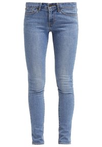 Jean slim bleu clair avec cinq poches, fermeture par bouton et légère décoloration sur les cuisses et les genoux.
