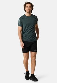 Mörkgrön kortärmad idrottströja med axelaccenter och svarta idrottsshorts. Texturerat tyg med fuktavvisande egenskaper.